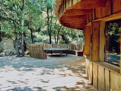 Cabane en bois dans les arbres, avec une terrasse en bois et un coin repas.