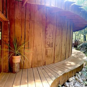 Cabane en bois ronde avec terrasse en bois, entourée de verdure.