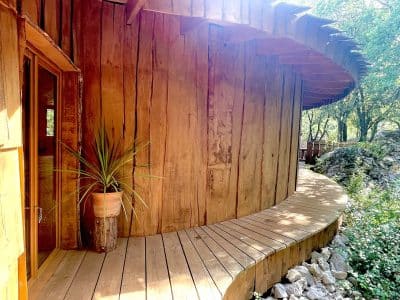 Cabane en bois ronde avec terrasse en bois, entourée de verdure.