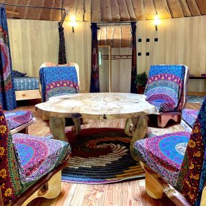 Hébergement insolite en yourte, intérieur chaleureux avec sièges colorés et table en bois.