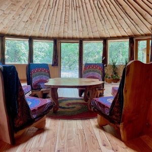 Yourte spacieuse en bois avec chaises colorées et vue sur la nature environnante.