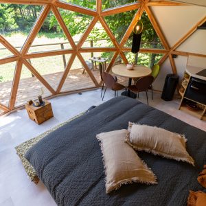 Dôme géodésique en bois avec vue sur la nature, lit confortable et coin repas.
