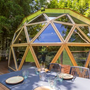 Hébergement insolite en dôme géodésique, entouré de verdure, avec une terrasse accueillante.