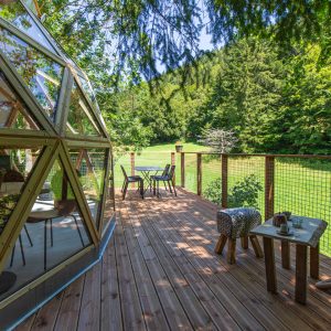 Dôme géodésique en bois avec terrasse en bois, entouré de verdure en Auvergne.