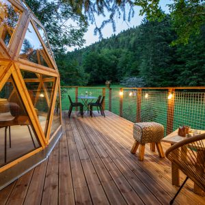 Dôme en bois avec terrasse, entouré de verdure, idéal pour un séjour insolite.