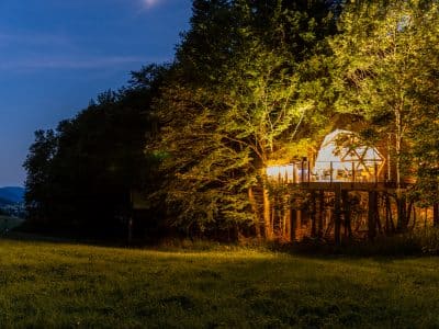 Cabane perchée dans les arbres, illuminée, entourée de verdure en Auvergne-Rhône-Alpes.