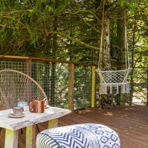 Cabane perchée en Auvergne-Rhône-Alpes, avec terrasse en bois et fauteuil suspendu.