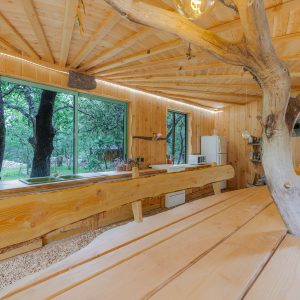 Cabane en bois dans les arbres, avec un grand table en bois et des fenêtres lumineuses.
