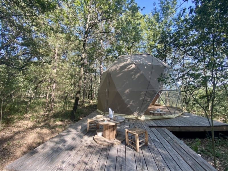 Dôme géodésique en pleine nature, avec terrasse en bois et vue sur la forêt.