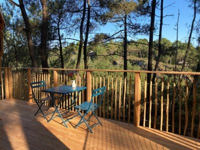 Cabane perchée en Bretagne avec terrasse en bois et vue sur la forêt verdoyante.