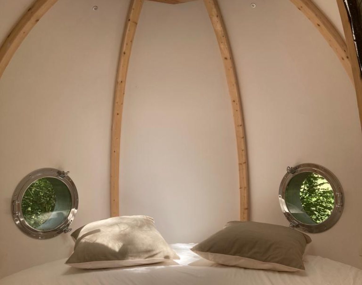 Hébergement insolite en forme de bulle, avec un toit en bois et fenêtres rondes.