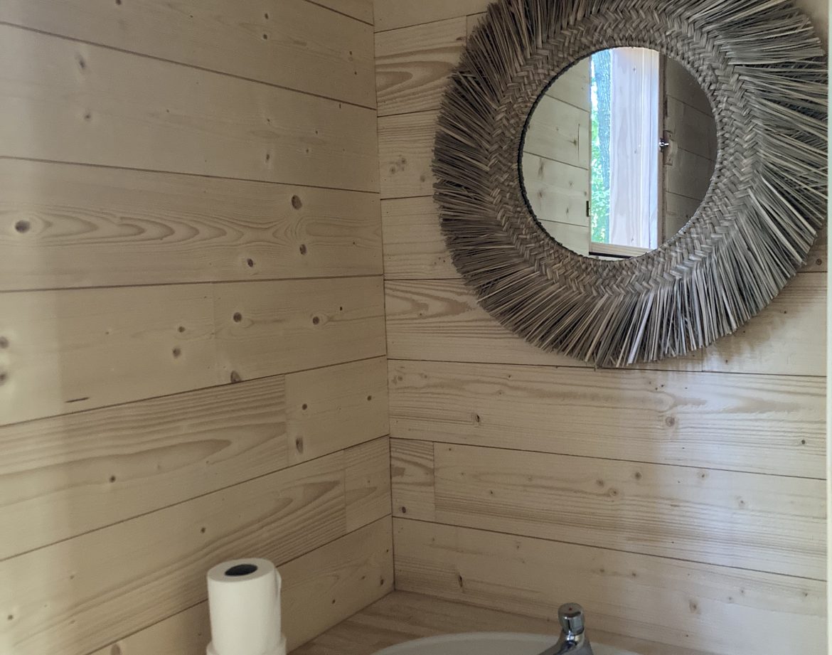 Salle de bain en bois dun hébergement insolite à Pays de la Loire, miroir rond en paille.