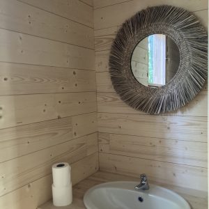 Salle de bain en bois dun hébergement insolite à Pays de la Loire, miroir rond en paille.