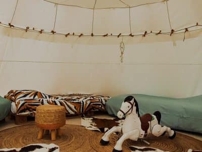 Tente safari cosy à Champagne-Ardenne, avec tapis en jute et cheval à bascule.