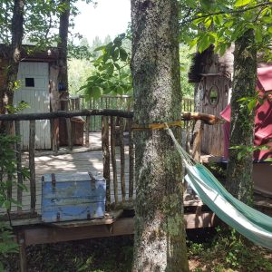Cabane perchée dans les arbres, avec une terrasse en bois et un hamac suspendu.