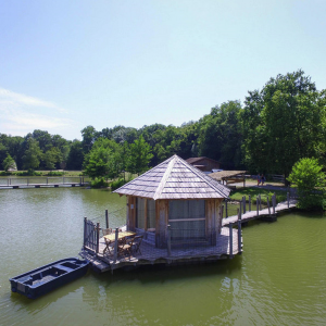 Cabane flottante au bord dun lac, entourée de verdure et dun pont en bois.