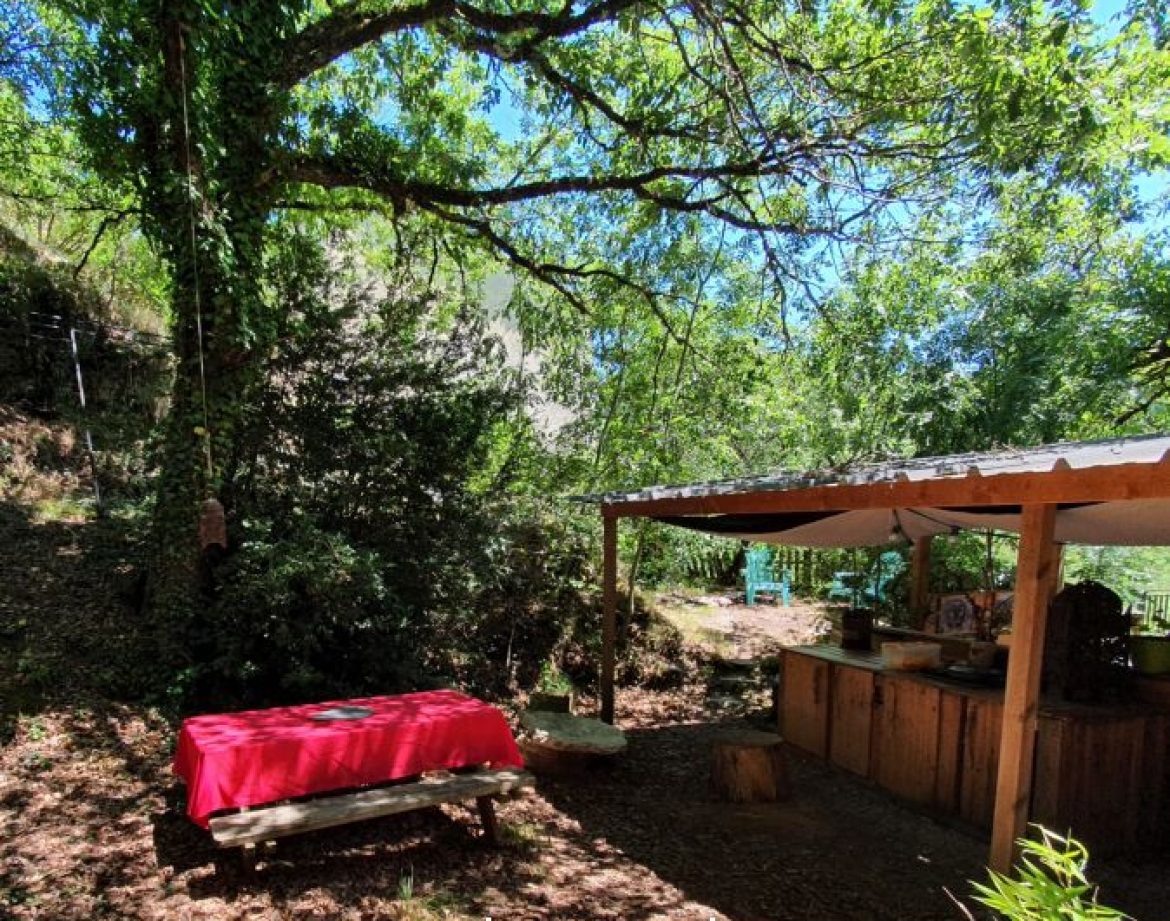 Cabane insolite en Languedoc-Roussillon, sous un arbre avec table en bois et coin cuisine.