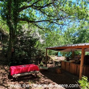 Cabane insolite en Languedoc-Roussillon, sous un arbre avec table en bois et coin cuisine.
