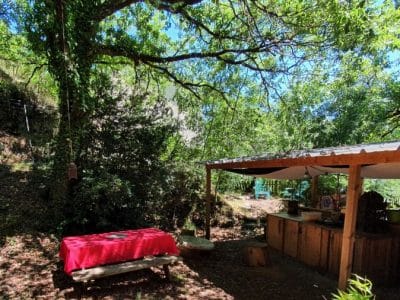 Cabane insolite en Languedoc-Roussillon, sous un arbre avec table en bois et coin cuisine.