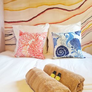 Chambre cosy dans un hébergement insolite, avec coussins colorés et serviettes douces.