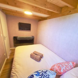 Chambre cosy en hébergement insolite, avec poutres apparentes et coussins colorés.