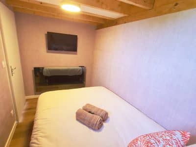 Chambre cosy en hébergement insolite, avec poutres apparentes et coussins colorés.