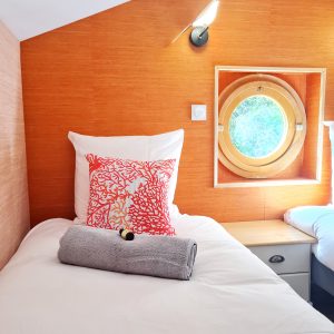 Chambre dans un hébergement insolite avec mur orange et hublot rond.