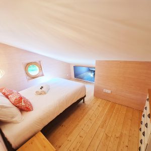 Chambre dans un hébergement insolite avec fenêtre ronde et décoration chaleureuse.