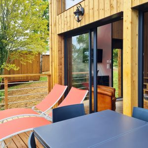 Hébergement insolite en bois avec terrasse, chaises longues et vue sur la nature.