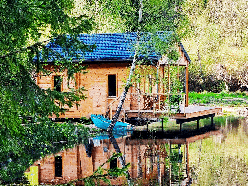 Cabane en bois au bord dun étang, avec un kayak bleu sur la terrasse.