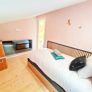 Chambre cosy dans un hébergement insolite, murs roses et lit en bois élégant.