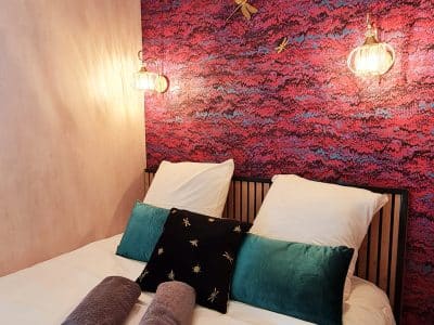 Chambre cocooning dans un hébergement insolite, mur coloré et luminaires élégants.