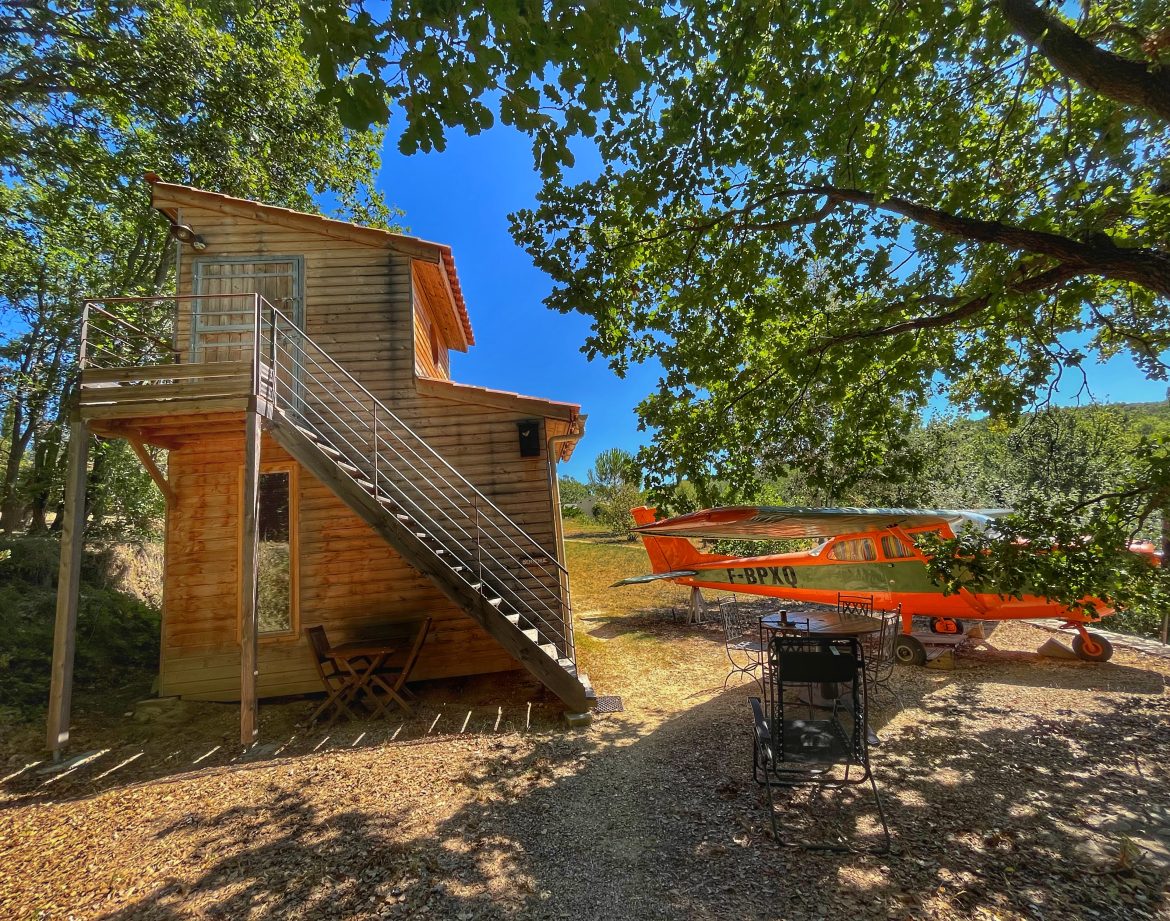 Cabane en bois avec un avion orange, entourée darbres au Languedoc-Roussillon.