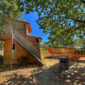 Cabane en bois avec un avion orange, entourée darbres au Languedoc-Roussillon.