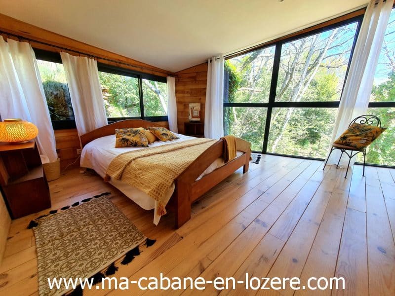 Chalet en bois lumineux avec vue sur la nature, lit douillet et décoration chaleureuse.