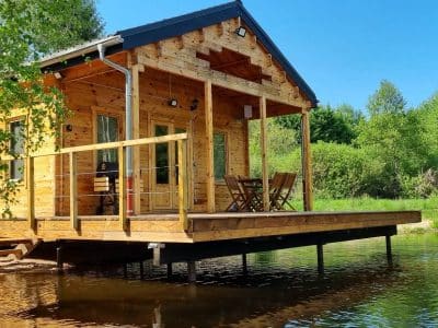 Cabane en bois sur pilotis, entourée de verdure et reflétant dans leau.