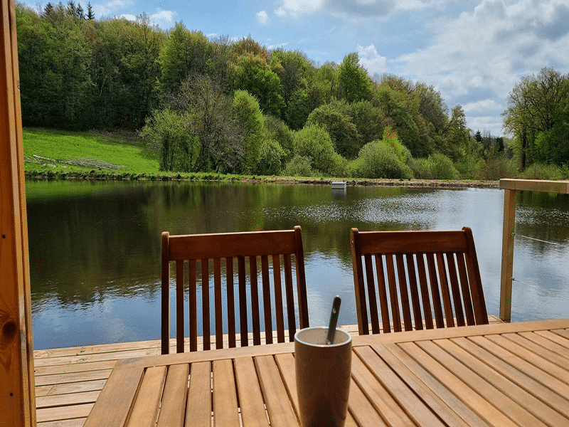 Chalet au bord de leau avec vue sur la nature verdoyante et un café sur la table.