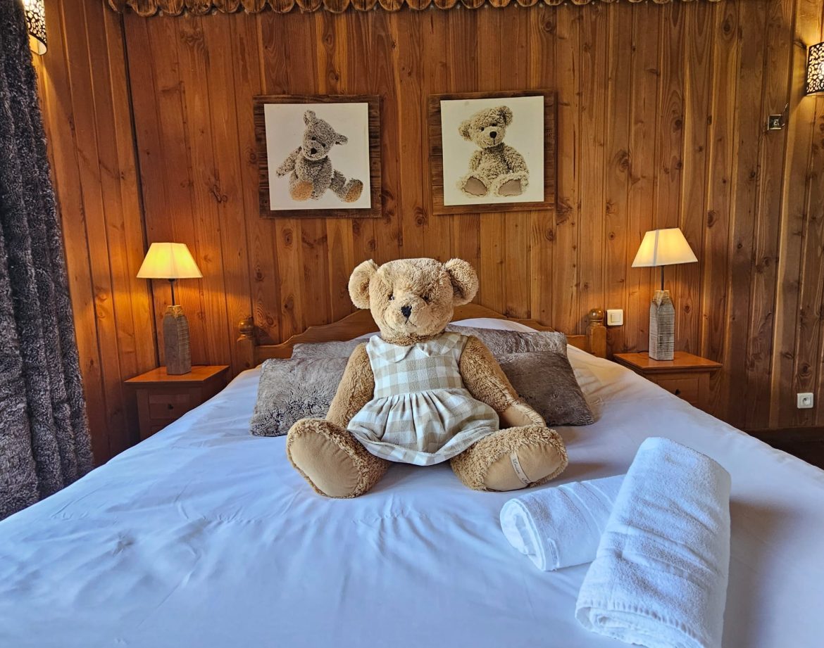 Chalet en bois douillet avec ours en peluche sur le lit et lampes chaleureuses.