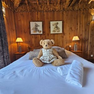 Chalet en bois douillet avec ours en peluche sur le lit et lampes chaleureuses.