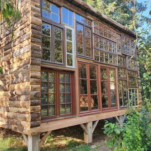 Cabane en bois avec de nombreuses fenêtres, nichée dans la verdure de Nouvelle-Aquitaine.