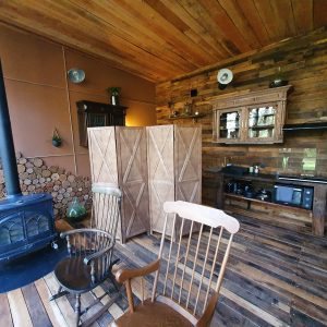 Hébergement insolite en bois avec poêle à bois et cuisine ouverte, ambiance chaleureuse.