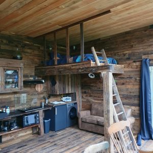 Cabane en bois avec mezzanine, intérieur chaleureux et cuisine équipée.