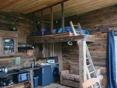 Cabane en bois avec mezzanine, intérieur chaleureux et cuisine équipée.
