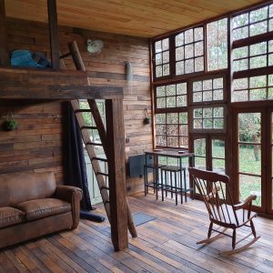 Hébergement insolite en bois avec mezzanine et grandes fenêtres sur la nature.