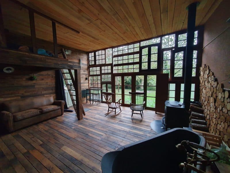 Hébergement insolite en bois avec grandes fenêtres et coin salon chaleureux.