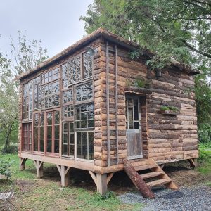Cabane en bois unique avec de grandes fenêtres, nichée dans la verdure de Nouvelle-Aquitaine.