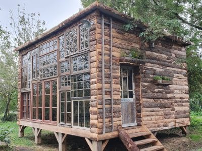 Cabane en bois unique avec de grandes fenêtres, nichée dans la verdure de Nouvelle-Aquitaine.