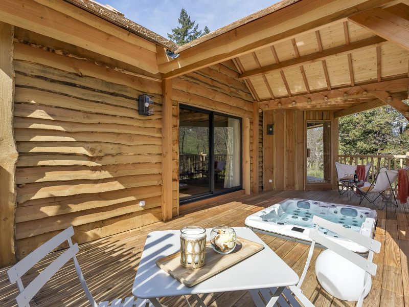 Chalet en bois avec terrasse, jacuzzi et mobilier extérieur accueillant.