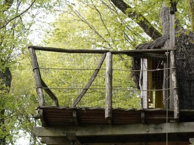 Cabane perchée en bois avec balcon, entourée de verdure en Bourgogne-Franche-Comté.