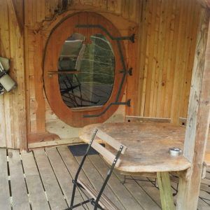 Cabane en bois avec une porte ronde et une table en bois sur la terrasse.
